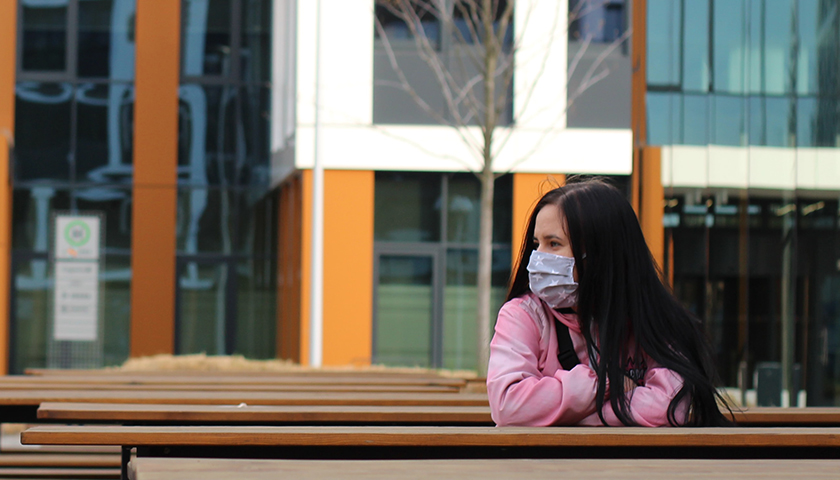 Woman sitting alone with a mask on.