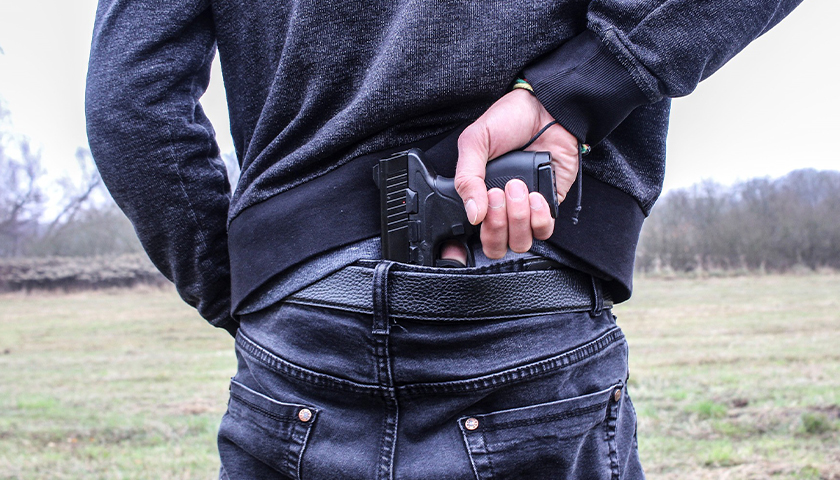 Guy grabbing handgun out of back of pants
